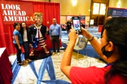 Peserta konferensi berpose di samping patung mantan presiden AS Donald Trump pada pameran CPAC di Orlando, Florida, 27 Februari 2021. (AP Photo / John Raoux)