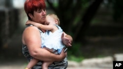 An unidentified refugee woman, carries a young girl, near a dormitory, after being displaced due to shelling, in the city of Donetsk, eastern Ukraine, July 13, 2014. 