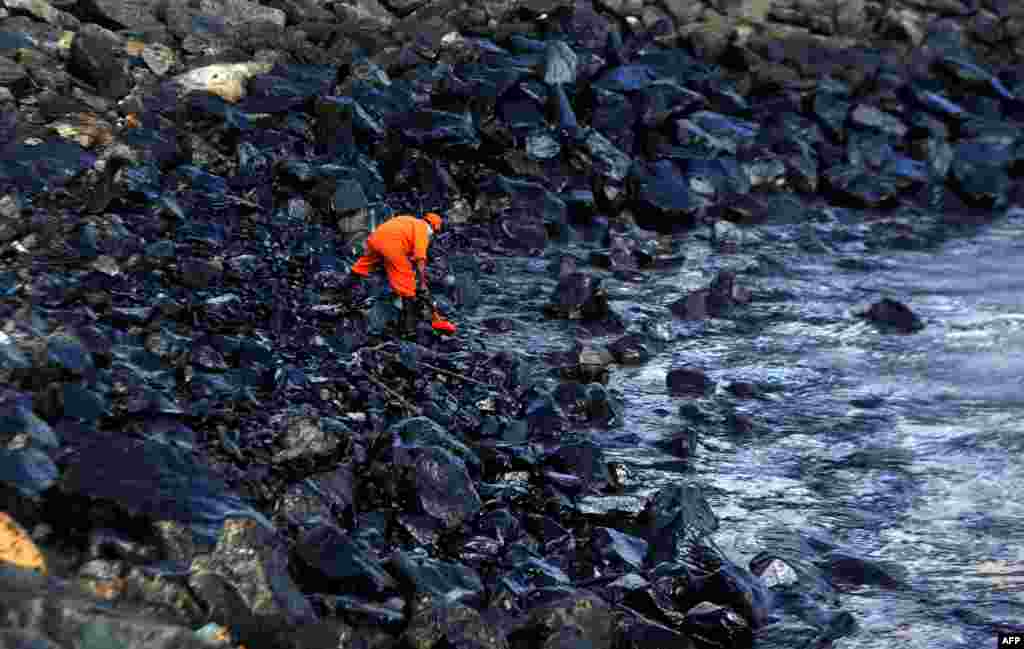 A member of the Pollution Response Team collects a sample of an oil spill from boulders at the coast, a day after an oil tanker and an LPG tanker collided off Kamarajar Port in Ennore, in Chennai, India.