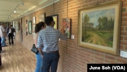 Visitors study some of the works on display in the refugee exhibit at the Sandy Spring Museum in Maryland. Many of the works depict scenes from the artists' home countries.