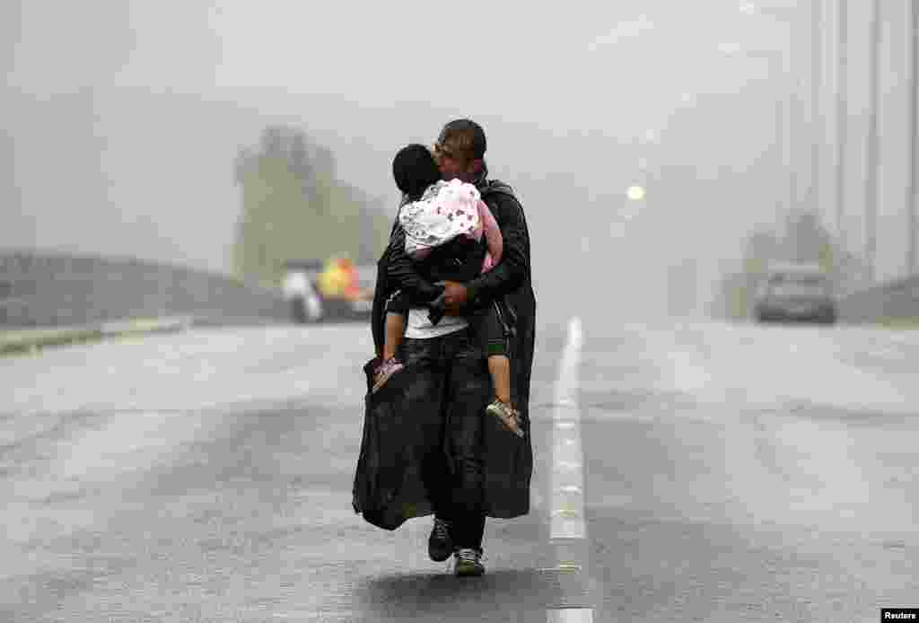 A Syrian refugee kisses his son as he walks through a rainstorm towards Greece&#39;s border with Macedonia, near the Greek village of Idomeni.