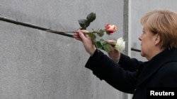 ဂျာမနီဝန်ကြီးချုပ် Angela Merkel places ဘာလင်တံတိုင်းလက်ကျန်နေရာမှာ အမှတ်တရနှင်းဆီ ထိုးပေးစဉ်။ (နိုဝင်ဘာ ၉၊ ၂၀၁၄)