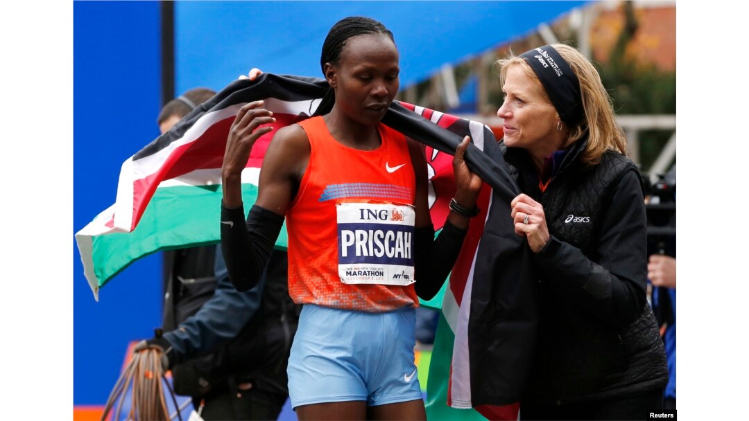 Priscah Jeptoo (L) of Kenya is wrapped in the Kenyan flag by Mary Wittenberg, president of the New York Road Runners, after Jeptoo crossed the finish line to win the women's division of the New York City Marathon, Nov. 3, 2013.
