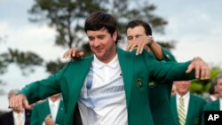 Defending Masters' champion Adam Scott, of Australia, helps Bubba Watson, left, with his green jacket after winning the Masters golf tournament Sunday, April 13, 2014.