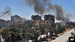 In this July 7, 2013, citizen journalism image provided by Lens Young Homsi, black smoke rises from buildings damaged by Syrian government airstrikes and shelling in Homs, Syria.