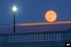 Traffic streaks by the supermoon as it rises behind the Memorial Bridge in Washington, Saturday, July 12, 2014. The full moon Saturday may seem huge, but it's just an illusion caused by its position in the sky. (AP Photo/J. David Ake)