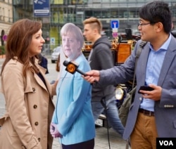 A foreign reporter interviews a local German journalist in Berlin on what reactions she has been getting to ‘Angela Merkel.’ “Most people laugh,” she says. (Photo: J. Dettmer / VOA)