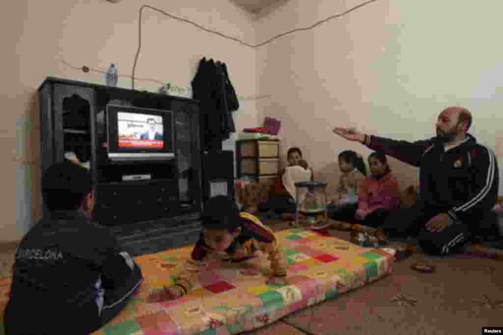 Syrian refugees who fled the violence in Syria watch Syria's President Bashar al-Assad speaking in Damascus, on a television at their temporary home at Al Hussein Palestinian refugees camp in Amman January 10, 2012.