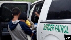 FILE - Families who crossed the nearby U.S.-Mexico border near McAllen, Texas, are placed in a Border Patrol vehicle, March 14, 2019. U.S. border authorities have increased the biometric data they take from children 13 and younger.