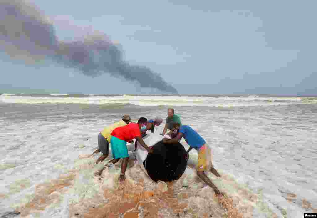 Smoke rises from a fire onboard the MV X-Press Pearl container ship in the seas off the Colombo Harbor as villagers push the cargo spilled from it on a beach in Ja-Ela, Sri Lanka.