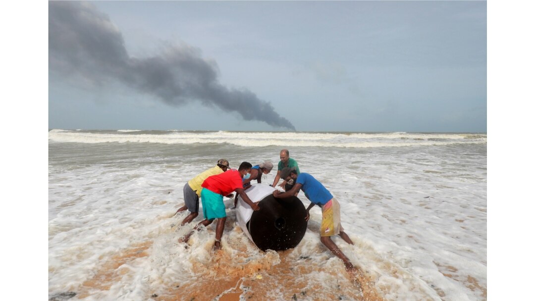 Asap mengepul dari api di atas kapal kontainer MV X-Press Pearl di laut lepas Pelabuhan Kolombo saat penduduk desa mendorong kargo yang tumpah darinya di pantai di Ja-Ela, Sri Lanka 26 Mei 2021. (Foto: Reuters)