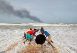 Asap mengepul dari api di atas kapal kontainer MV X-Press Pearl di laut lepas Pelabuhan Kolombo saat penduduk desa mendorong kargo yang tumpah darinya di pantai di Ja-Ela, Sri Lanka 26 Mei 2021. (Foto: Reuters)