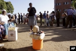 A Zimbabwean woman, left, sells slices of bread to people in a queue on election day in Harare, Saturday, March, 29, 2008.