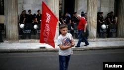 A refugee child holds a flag during a protest, called by the 'United against Rascism and the Fascist Threat' movement, demanding better conditions for refugees in the Greek camps, in front of the City Hal in Athens, June 9, 2016.