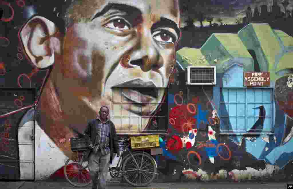Un homme &nbsp;s&#39;éloigne de sa bicyclette arrêtée contre une peinture murale du président Barack Obama, créée par l&#39;artiste Bankslave au Centre des arts de GoDown à Nairobi , au Kenya, le 22 juillet 2015.