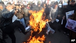 FILE - Followers of Shiite cleric Muqtada al-Sadr burn an effigy of King Salman of Saudi Arabia as they hold posters of Sheik Nimr al-Nimr during a demonstration in Baghdad, Iraq, Jan. 4, 2016.