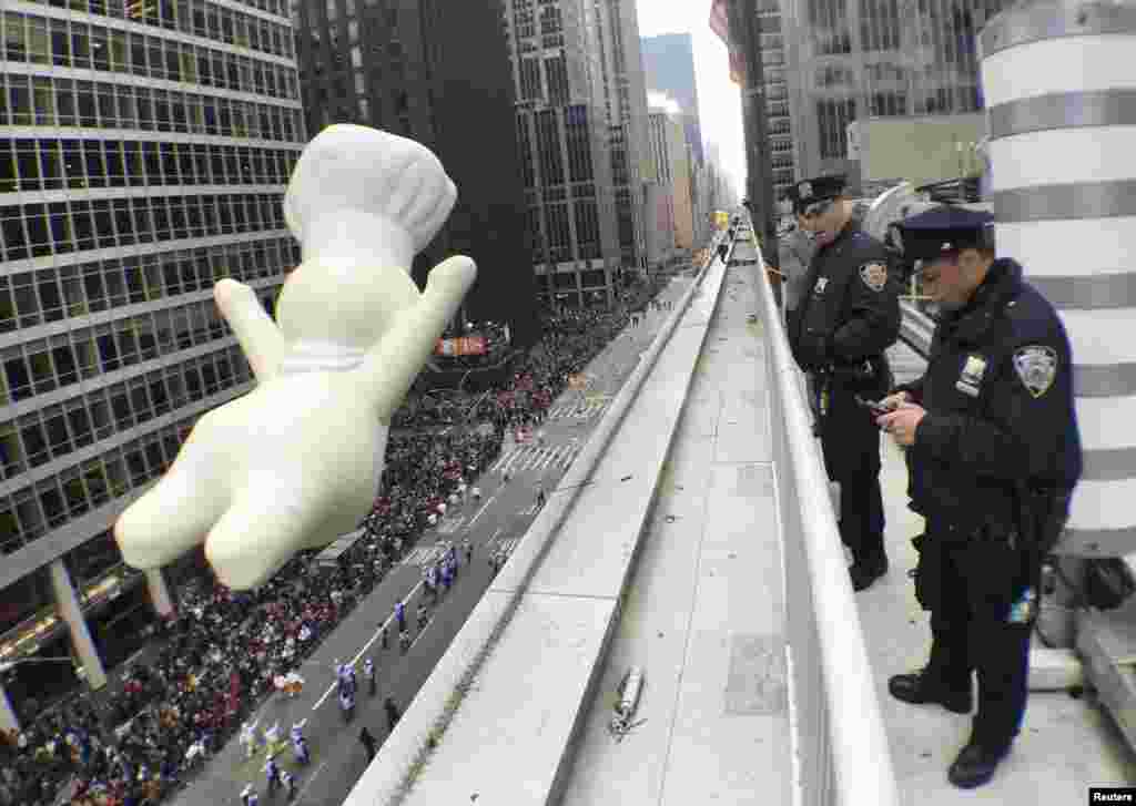 New York Police Department officers stand watch from a building as a float proceeds high above spectators along 6th Ave during the 89th Macy&#39;s Thanksgiving Day Parade in the Manhattan borough of New York.