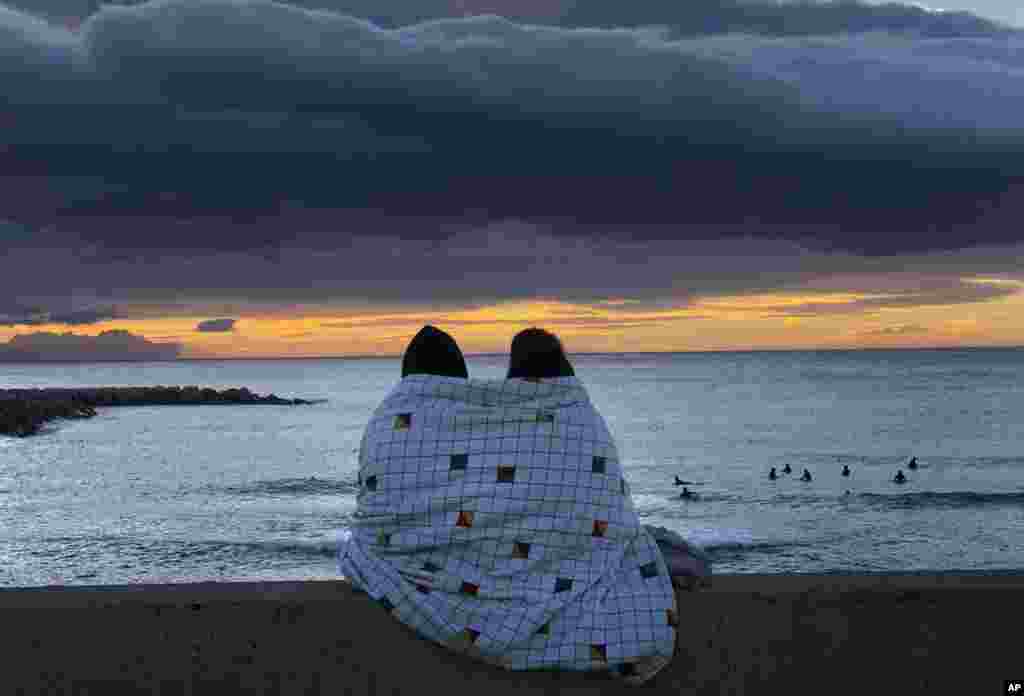 A couple watch the sunrise in front of the Mediterranean Sea in Barcelona, Spain.