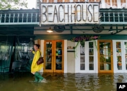 Aimee Cutter, pemilik restoran Beach House, berjalan dalam genangan banjir dari Danau Pontchartrain di Lakeshore Drive, Mandeville, La., 13 Juli 2019. (Foto: dok).