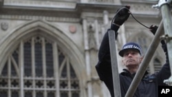 As part of security preparations for the upcoming royal wedding, a British police officer uses a micro-camera to inspect the inner tubes of a scaffolding reserved for media, outside Westminster Abbey, background, in central London, Tuesday, April 26, 2011