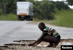 FILE - A woman gathers grain spilled by cargo trucks from Zambia along a highway in Magunje, Zimbabwe, Feb. 20, 2016. Zimbabwean President Robert Mugabe had declared a state of disaster in most rural parts of the country severely hit by a drought.