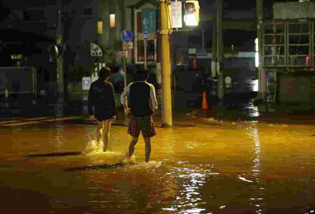 People walk through a flooded street in Joso, Ibaraki prefecture, north of Tokyo, Thursday, Sept. 10, 2015. Raging floodwaters broke through a flood berm Thursday and swamped the city north of Tokyo, washing away houses, forcing dozens of people to roofto