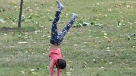 A young girl walks on her hands through the grass.