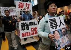 FILE - A protester wearing a mask of bookseller Lee Bo stands in a cage during a protest against the disappearances of booksellers in Hong Kong, Jan. 10, 2016.