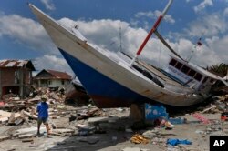 Seorang warga desa Wani di pinggiran Palu, Sulawesi Tengah, Rabu, 10 Oktober 2018, berjalan melewati sebuah perahu yang tersapu ke pantai akibat tsunami.