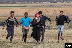 FILE - Palestinian protesters hold hands to protect a girl from shots as they run for cover during clashes with Israeli security forces following a demonstration near the border with Israel, east of Khan Yunis, in the southern Gaza Strip on March 31, 2018.