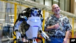Marc Raibert, founder and chair of Boston Dynamics stands beside one of the company's Atlas robots during an interview and demonstration, Wednesday, Jan. 13, 2021, at their facilities in Waltham, Mass. (AP Photo/Josh Reynolds)