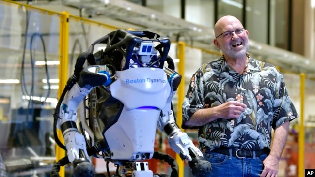 Marc Raibert, founder and chair of Boston Dynamics stands beside one of the company's Atlas robots during an interview and demonstration, Wednesday, Jan. 13, 2021, at their facilities in Waltham, Mass. (AP Photo/Josh Reynolds)