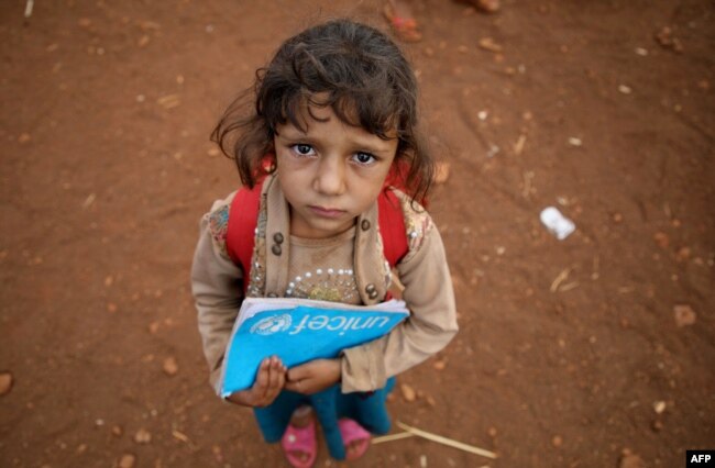 FILE - A Syrian child holds a book in the yard of a makeshift school in al-Jeneinah camp for displaced people in the village of Atme, in Syria's mostly rebel-held northern Idlib province.