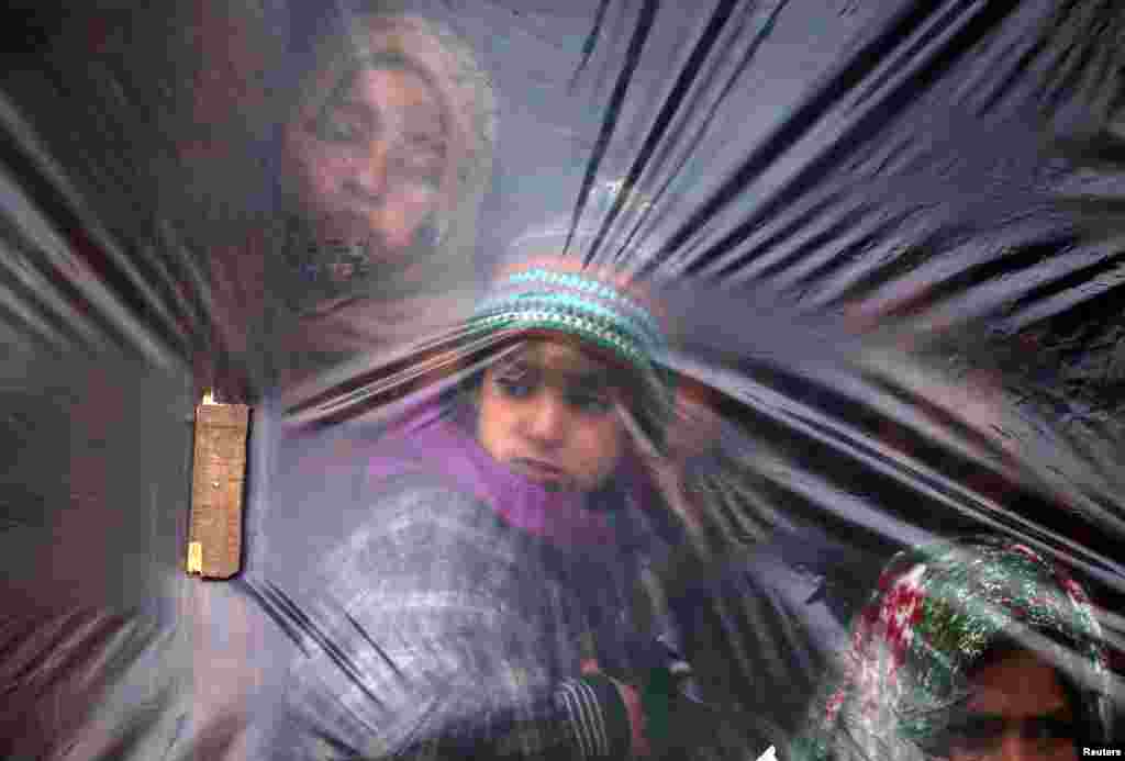Children look out from a window, covered with a plastic sheet to protect from cold, on a winter day in a village of south Kashmir&#39;s Pulwama district, India.