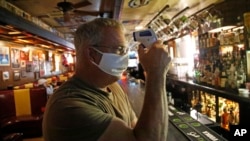 Cheers to You bar owner Bob Brown tests a thermometer at his bar Friday, May 1, 2020, in Salt Lake City. Brown realize he needs to hire two or three new people just to enforce social distancing guidelines. (AP Photo/Rick Bowmer)