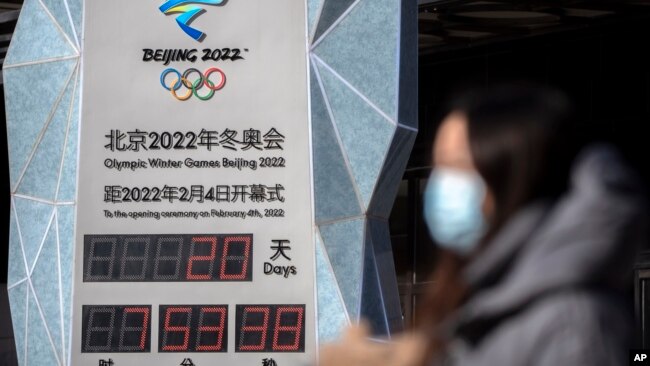 A woman wearing a face mask to protect against COVID-19 walks past a clock counting down the time until the opening ceremony of the 2022 Winter Olympics in Beijing, Jan. 15, 2022.