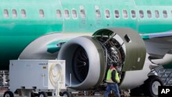 FILE - A worker walks past an engine on a Boeing 737 MAX 8 airplane being built for American Airlines at Boeing Co.'s Renton assembly plant, March 13, 2019, in Renton, Wash.