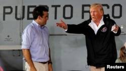 U.S. President Donald Trump talks with Puerto Rico Governor Ricardo Rossello, left, as they take their seats for a briefing on hurricane relief efforts at Muniz Air National Guard Base in Carolina, Puerto Rico, Oct. 3, 2017.