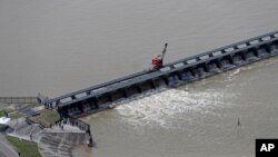 FILE - Workers open the gates of the Bonnet Carre spillway, a river diversion structure, which diverts water from the rising Mississippi River, left, to Lake Pontchartrain, in Norco, La., March 8, 2018.