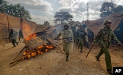 Riot police walk past burning barricades erected by protesters throwing rocks, during clashes in the Kawangware slum of Nairobi, Kenya, Aug. 10, 2017.
