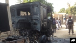 In this photo taken with an iPad policemen stand guard at a burned out truck following an attack by Boko Haram Islamists near an air force base in Maiduguri, Nigeria, Dec, 2. 2013.