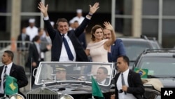 Diapit oleh Ibu Negara Michelle Bolsonaro, Presiden Brazil Jair Bolsonaro melambaikan tangan saat mengendarai mobil terbuka setelah upacara pelantikan di Brasilia, Brazil, 1 Januari 2018.
