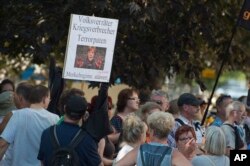 Demonstrators hold a poster with a photo of Angela Merkel and the writing 'Traitor, war criminal, terror godparent - the Merkel regime must go" during Merkel's visit to Dresden, eastern Germany, Aug. 16, 2018.