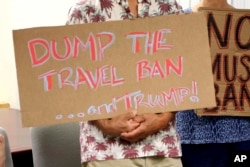 FILE - Critics of President Donald Trump's travel ban hold signs during a news conference with Hawaii Attorney General Douglas Chin, June 30, 2017 in Honolulu.