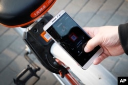 FILE - A commuter uses an app to unlock a bicycle from bike-sharing company Mobike in Beijing, China, March 29, 2017.