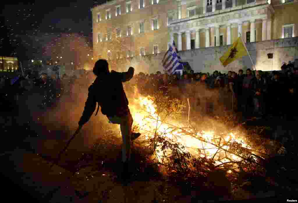 Seorang demonstran terlihat dekat api yang dinyalakan oleh para petani yang marah di luar parlemen pada unjuk rasa menentang reformasi pensiun di Athena, Yunani.