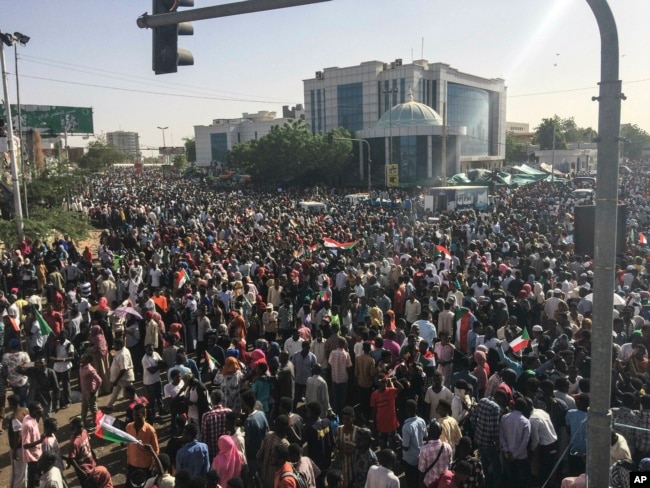 Sudanese demonstrators march with national flags as they gather during a rally demanding a civilian body to lead the transition to democracy, outside the army headquarters in the Sudanese capital Khartoum, April 13, 2019.