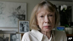 FILE - Author Joan Didion sits in front of a photo of herself holding her daughter, Quintana Roo, and another picture of her daughter's wedding, in her New York apartment Sept. 26, 2005. 
