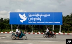 Men ride motorbikes past a billboard of the upcoming Union Peace Conference, Aug. 26, 2016, in Naypyitaw, Myanmar.