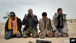 Libyan rebels pray in the desert in front a weapon on the frontline near Sultan, south of Benghazi, March 18, 2011